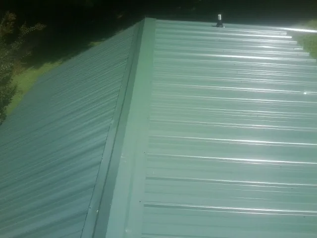 New green metal panels meeting at the ridge of a roof — Flat Roof Repair work by our crew in Mohawk